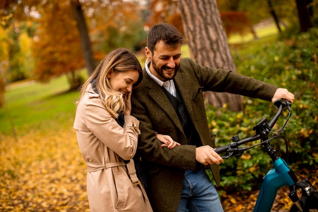 Jovem casal no parque outono com bicicleta elétrica