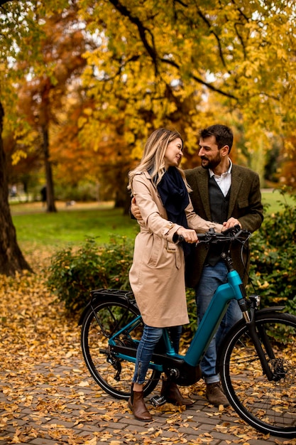 Jovem casal no parque outono com bicicleta elétrica