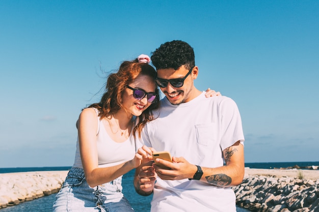 Jovem casal olha seu smartphone em frente à praia