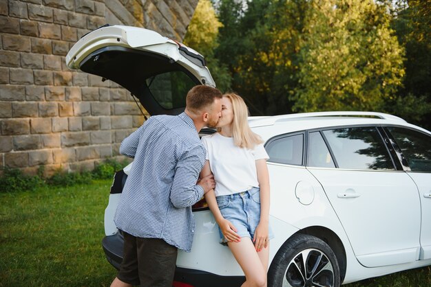 Jovem casal parado perto do porta-malas do carro aberto, olhando para a câmera, ao ar livre