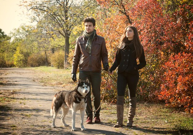 Jovem casal passeando com seu cachorro husky na zona rural de outono