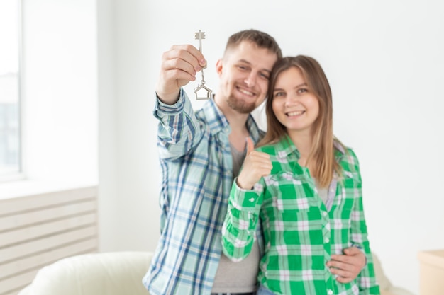 Foto jovem casal positivo segurando as chaves de um novo apartamento enquanto estava em sua sala de estar. conceito de hipoteca de inauguração de casa e família.