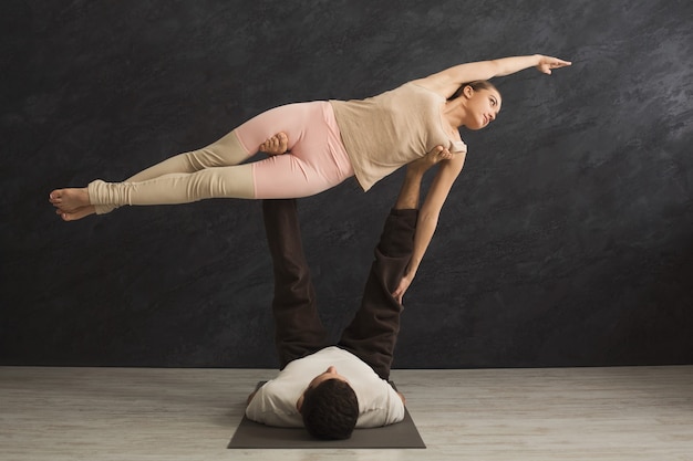 Foto jovem casal praticando acroyoga na esteira na academia juntos. mulher voando, cópia espaço, vista lateral. ioga de parceiro, flexibilidade, conceito de confiança