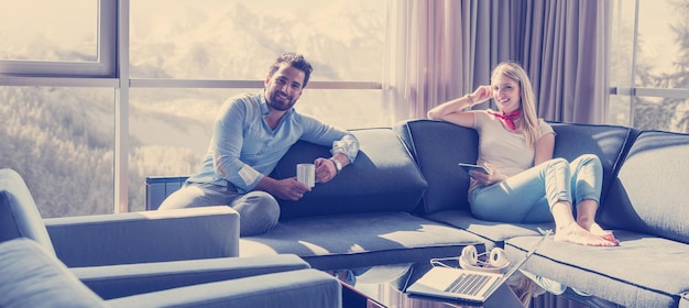 Jovem casal relaxando em casa usando computador tablet lendo na sala de estar perto da janela no sofá do sofá.