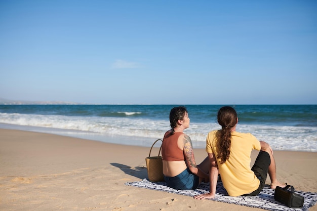 Jovem casal relaxando na praia sentado no cobertor e apreciando a vista para o mar