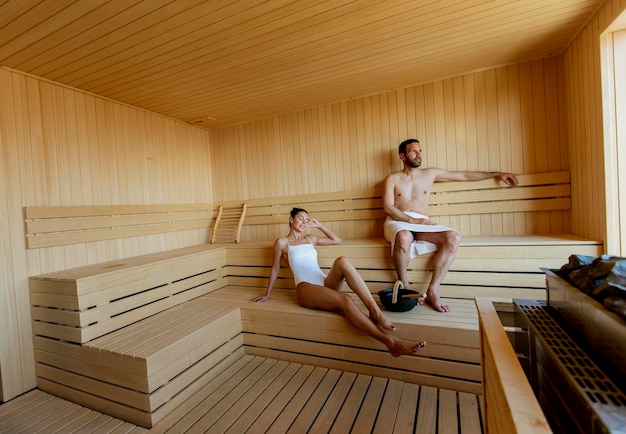 Jovem casal relaxando na sauna e assistindo a floresta de inverno pela janela