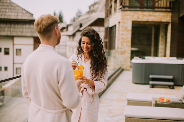 Jovem casal relaxando no terraço ao ar livre e bebendo suco de laranja fresco