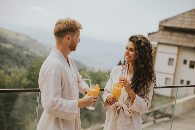 Jovem casal relaxando no terraço ao ar livre e bebendo suco de laranja fresco