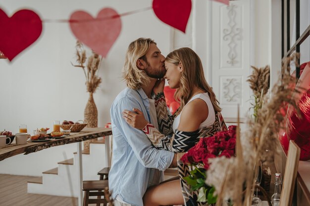 Foto jovem casal romântico abraçando e beijando enquanto comemorava aniversário de amor na casa decorada