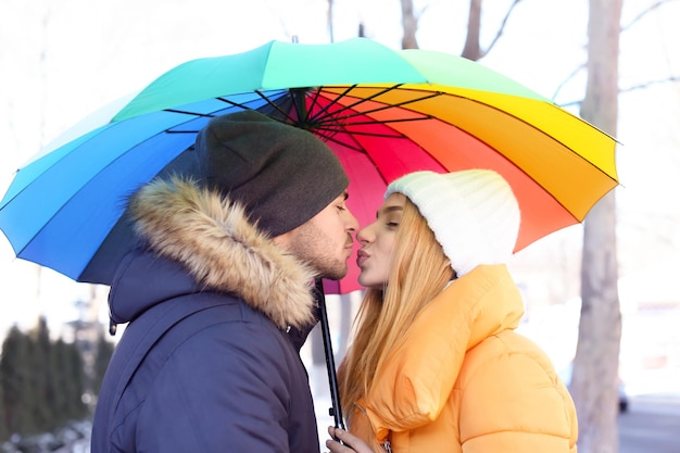 Jovem casal romântico com guarda-chuva colorido na rua da cidade