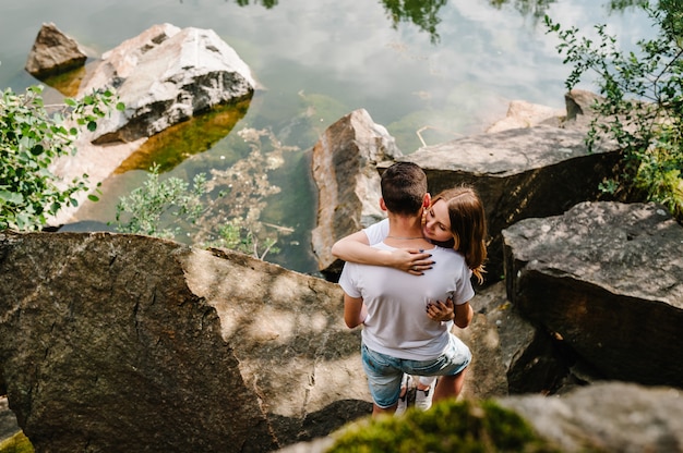 Jovem casal se abraçando em uma pedra perto do lago