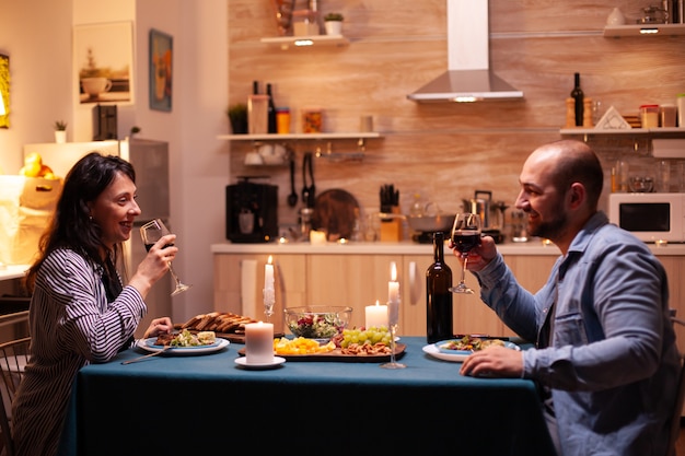 Jovem casal se divertindo durante o jantar. Casal feliz conversando, sentado à mesa na sala de jantar, apreciando a refeição, comemorando seu aniversário em casa tendo um tempo romântico.