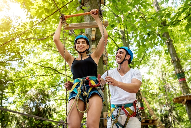 Jovem casal se divertindo no parque de corda aventura. Equipamento de escalada. Usar cinto de segurança e capacetes de proteção.