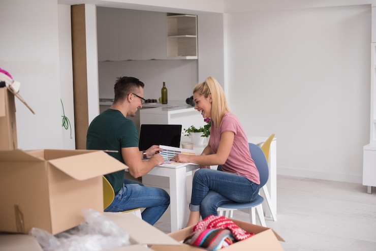 Foto jovem casal se mudando para uma nova casa. homem e mulher à mesa usando notebook e planos com caixas ao seu redor