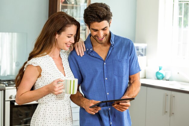 jovem casal segurando a xícara de café enquanto estiver usando tablet digital