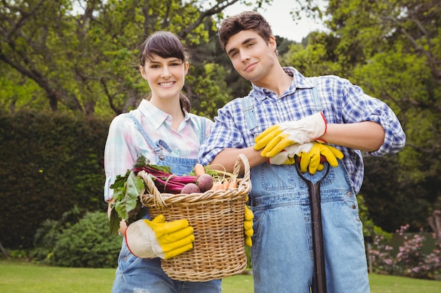 Jovem casal segurando uma cesta de legumes recém colhidos no jardim