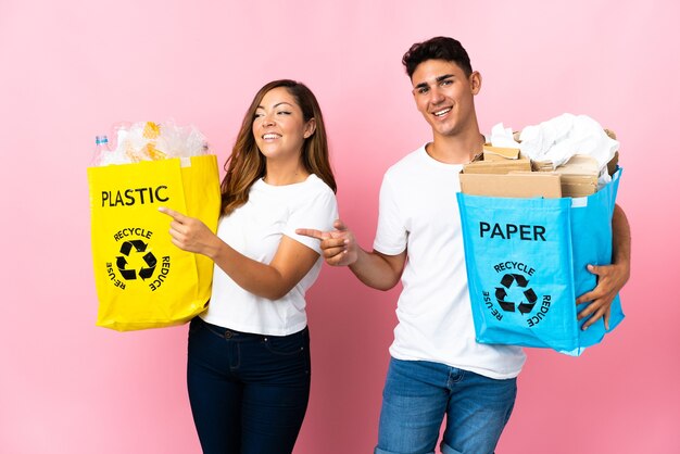 Jovem casal segurando uma sacola cheia de plástico e papel na rosa apontando o dedo para o lado