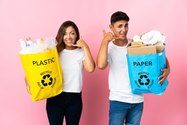 Jovem casal segurando uma sacola cheia de plástico e papel rosa, fazendo gestos de telefone. Ligue-me de volta sinal