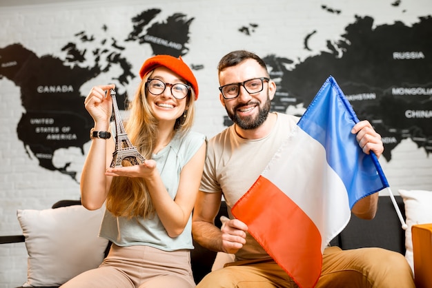 Jovem casal sentado com a torre eiffel e a bandeira da França no escritório da agência de viagens no plano de fundo do mapa mundial preparando-se para uma viagem a Paris