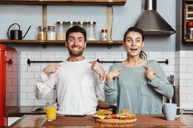 Jovem casal sentado na cozinha durante o café da manhã em casa, apontando o dedo um para o outro