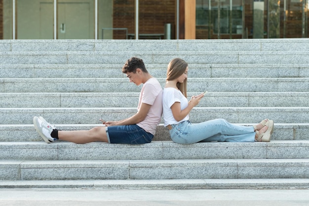 Jovem casal sentado nas escadas concentrado em seus telefones e mídias sociais