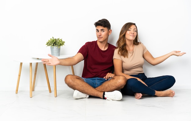 Foto jovem casal sentado no chão de branco estendendo as mãos para o lado para convidar para vir