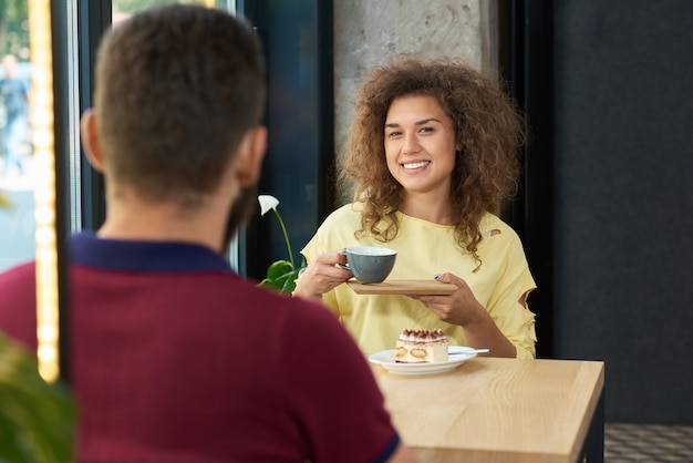 Jovem casal sentado no restaurante, bebendo café, sorrindo, falando.