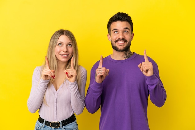 Jovem casal sobre fundo amarelo isolado apontando para cima com o dedo indicador uma ótima ideia