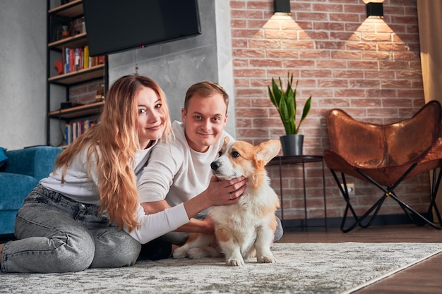 Jovem casal sorridente abraçando lindo cachorro em casa