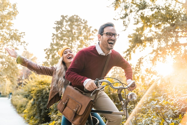 Jovem casal sorridente andando de bicicleta e desfrutando do outono no parque da cidade jovens atraentes rindo e dirigindo rápido sentindo liberdade