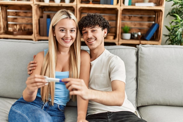 Jovem casal sorrindo feliz olhando resultado do teste de gravidez em casa