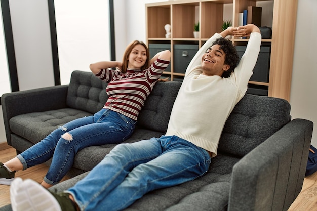 Jovem casal sorrindo feliz relaxado sentado no sofá em casa