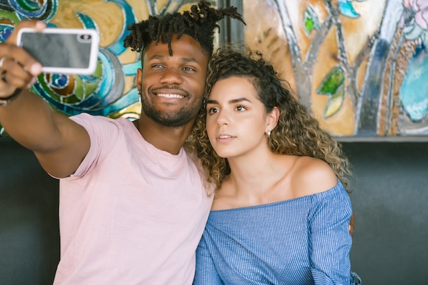 Jovem casal tirando uma selfie com um telefone celular enquanto está sentado em um restaurante.