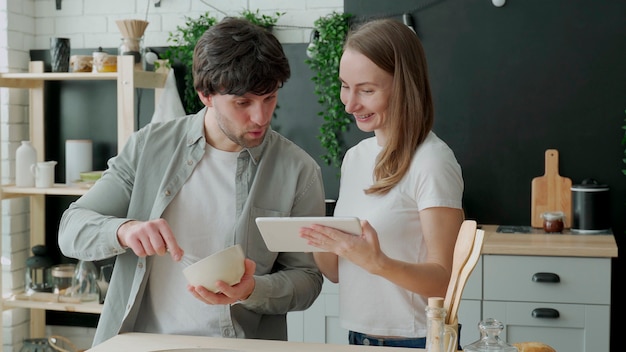 Jovem casal usa tablet digital e sorri enquanto cozinha na cozinha de casa