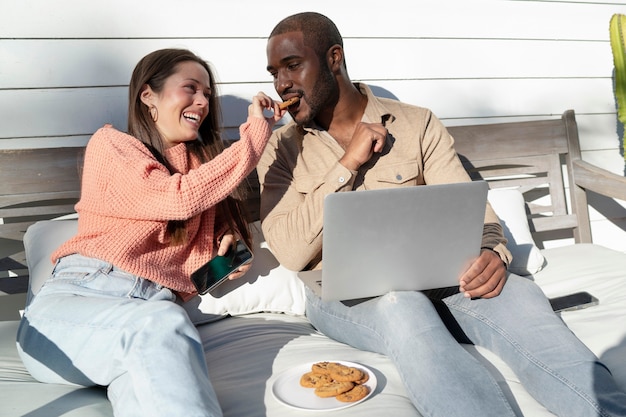 Foto jovem casal usando laptop juntos do lado de fora e comendo lanches