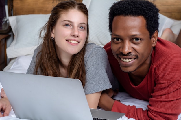 Jovem casal usando o laptop em uma cama em casa.