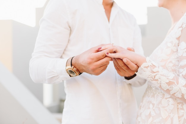 Jovem casal usando vestido de noiva branco e camisa, trocando alianças em sua cerimônia de casamento de sonho