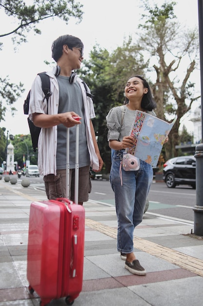 Jovem casal viajante em estilo casual usando mochila traz mala e câmera enquanto segura um mapa