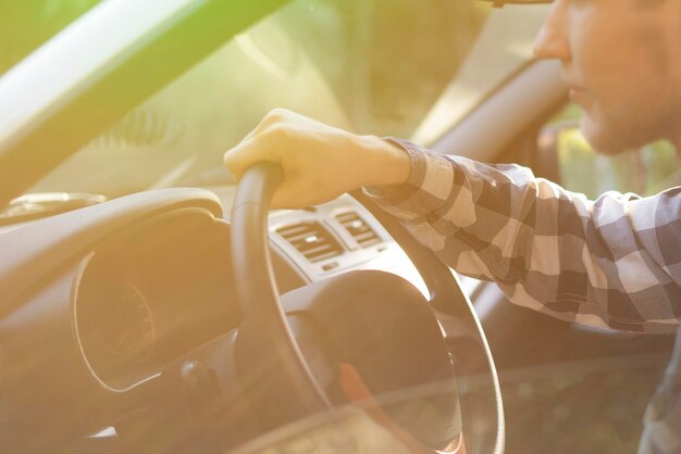 Jovem casual em camisa quadriculada dirigindo um carro durante o pôr do sol