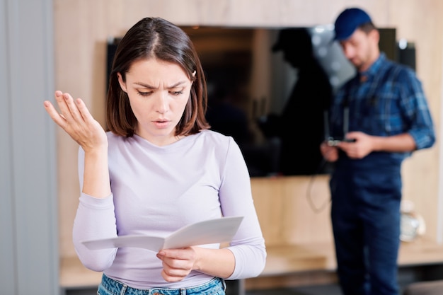 Jovem casual lendo instruções no folheto do guia de uso e expressando mal-entendido