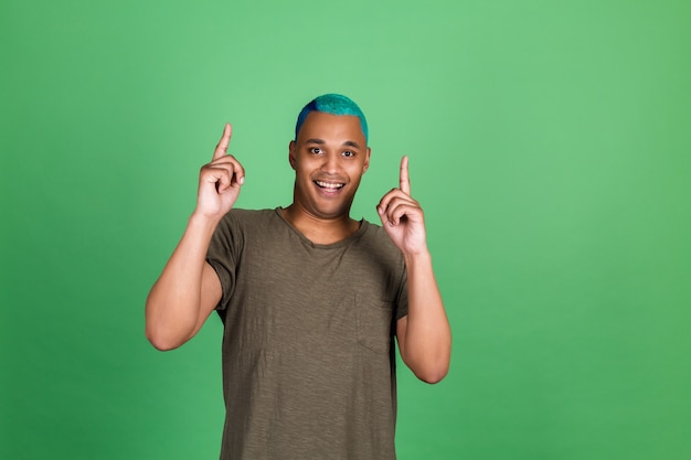 Jovem casual na parede verde cabelo azul alegre positivo apontar o dedo para cima