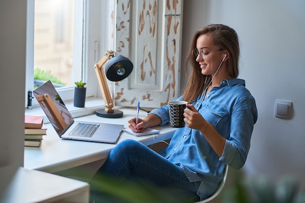 Jovem casual sorridente estudante inteligente em fones de ouvido, satisfeita com a aprendizagem de uma língua estrangeira.