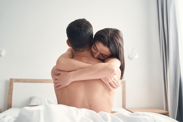 Jovem caucasiana apaixonada com cabelo comprido solto abraçando e beijando o marido na cama