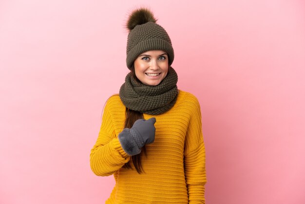 Jovem caucasiana com chapéu de inverno isolada em um fundo rosa com expressão facial surpresa