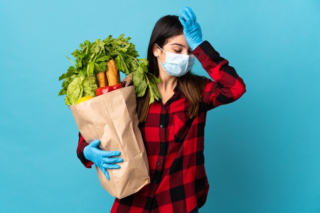 Jovem caucasiana com vegetais e máscara isolada na parede azul percebeu algo e pretende a solução