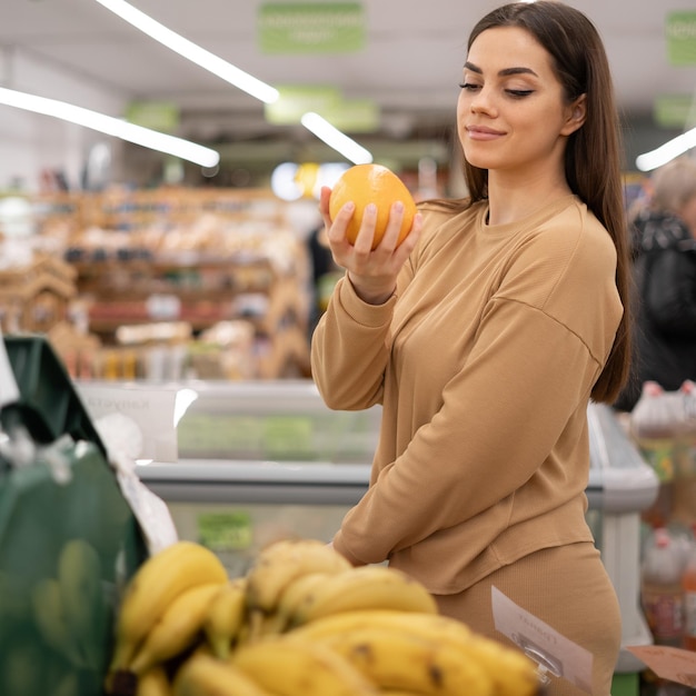 Jovem caucasiana em um supermercado compra uma laranja Uma mulher compra mantimentos e produtos básicos em uma loja orgânica local