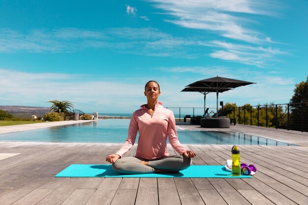 Foto jovem caucasiana praticando ioga e meditando perto da piscina. conceito de fitness e estilo de vida saudável