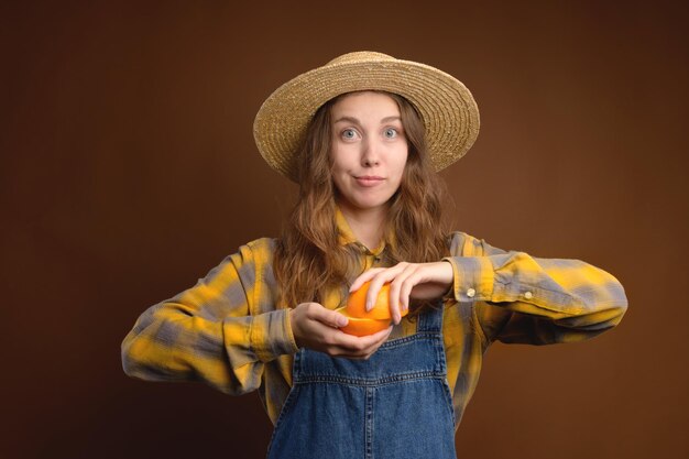 Foto jovem caucasiana rústica atraente com chapéu de palha segurando retrato de estúdio de frutas laranja cortadas