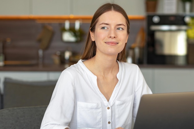 Jovem, caucasiana, sonhadora, com laptop, sentada à mesa, pensativa linda mulher olhando para o lado tentando apresentar seu futuro feliz