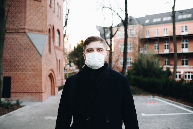 Jovem caucasiano andando lá fora usando máscara cirúrgica para proteger contra o coronavírus